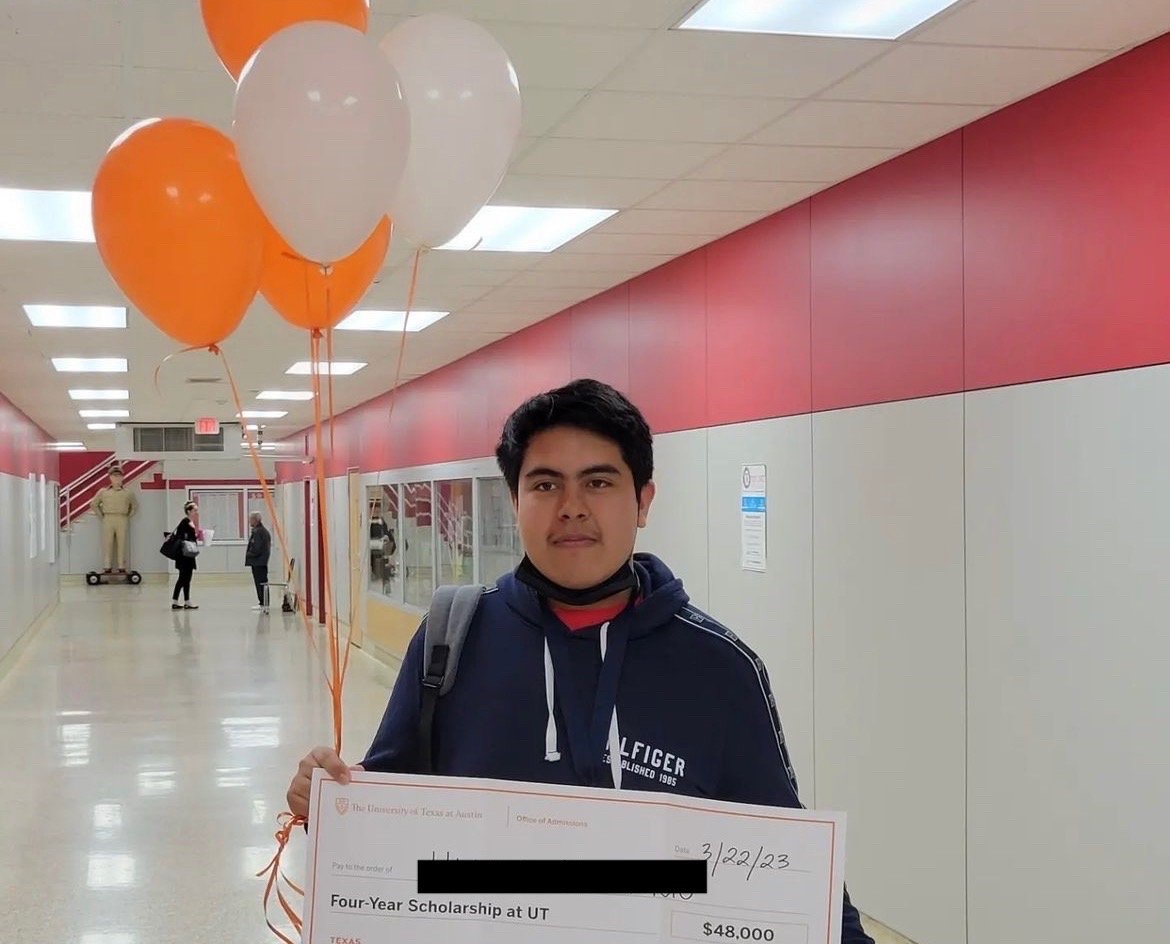 Student holding balloons and a UT Austin Four-Year Scholarship check in a school hallway